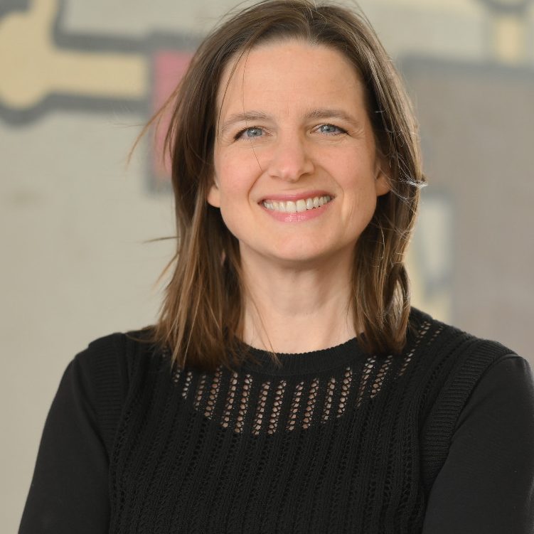 Julia Sittmann lächelt in die Kamera. Im Hintergrund ist ein Wandbild verschwommen zu sehen.