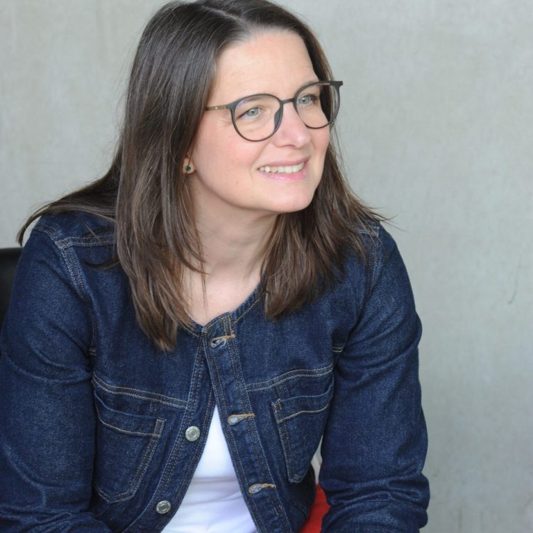 Julia Sittmann lächelt in die Kamera. Der Hintergrund ist hell und verschwommen.