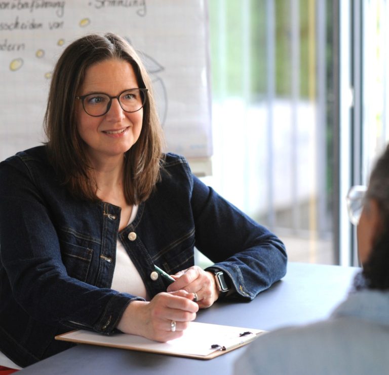 Julia Sittmann lächelt in die Kamera. Der Hintergrund ist hell und verschwommen.