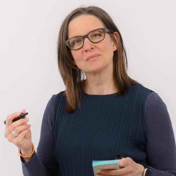 Julia Sittmann, Coach Julia Sittmann lächelt in die Kamera. Der Hintergrund ist hell und verschwommen.